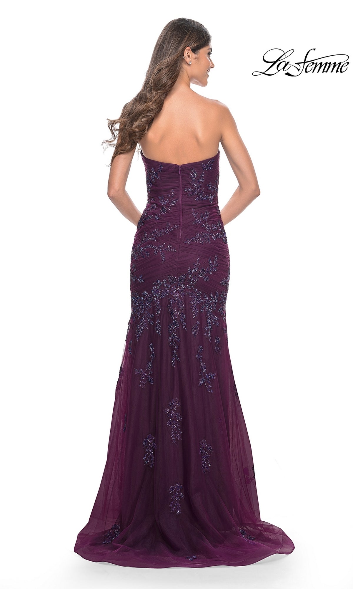 A woman with long brown hair wears the La Femme Strapless Long Mermaid Prom Dress 32121 in deep purple, featuring floral embroidery, a fitted bodice, and a graceful floor-length train.